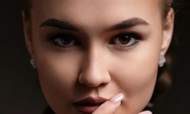 Gros plan sur un visage féminin aux **sourcils droits** et maquillés. Elle porte des boucles d'oreilles discrètes.