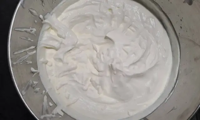 Crème fouettée onctueuse dans un bol en métal, prête à garnir un délicieux gâteau.