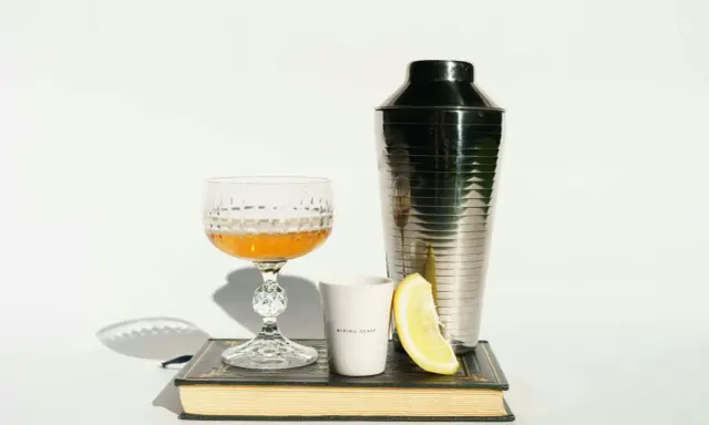 Szklanka z drinkiem, shaker, cytryna i książka. Idealne akcesoria, by dowiedzieć się, z czym pić amarula.