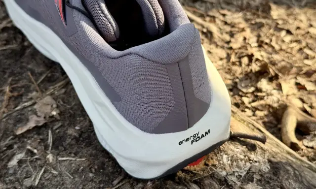 Szary but Salomon Ultra Glide 3 z białą podeszwą i napisem "energy FOAM" na tle leśnej ściółki.