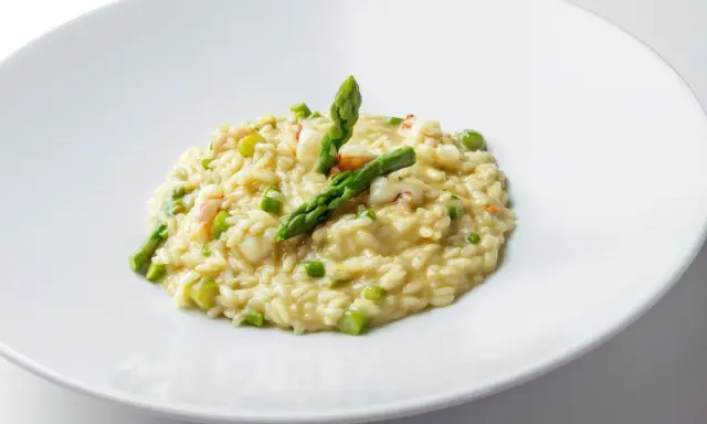 Risotto cremoso con asparagi freschi e succulenti gamberetti, guarnito con punte di asparagi croccanti.