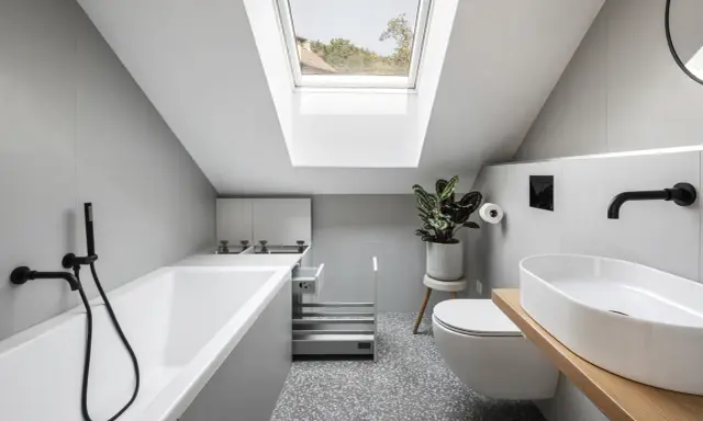 Un piccolo bagno sottotetto basso con vasca, WC, lavabo e lucernario.