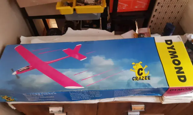 DYMOND RC-Flugzeug-Karton mit pinkem Modell. Ein gelber Streifen mit dem Schriftzug DYMOND.
