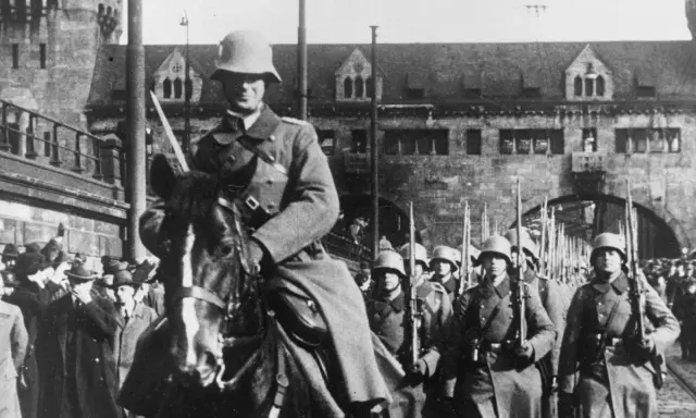 Soldaten marschieren in Formation, ein Reiter führt sie an. Ein historisches Bild der Rheinlandbesetzung 1936.