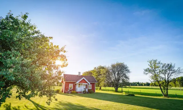 Czerwony domek na wsi, marzenie o własnym miejscu. Czy na działce rolnej można postawić domek do 70m2? Słoneczny dzień, zieleń i spokój.