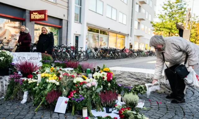 En kvinna lägger blommor vid en minnesplats för Kim Larsen. Många blommor och ljus.