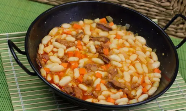 Alubias con chorizo y verduras en una paellera, plato tradicional español.