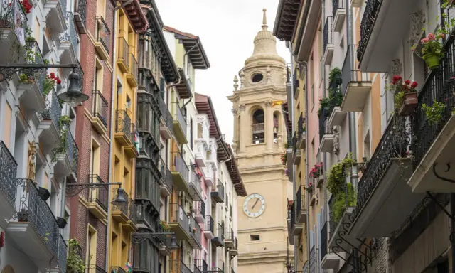 Edificio con balcónes floridos y torre de iglesia en Navarra. ¿Buscas ayudas cambio ventanas Navarra?