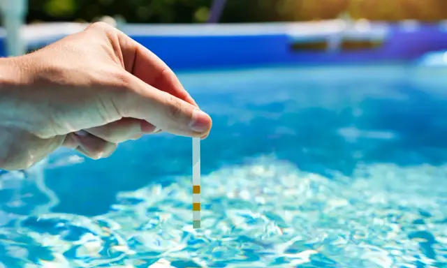 Main tenue une bandelette de test dans l'eau d'une piscine pour vérifier la qualité de l'eau, essentielle au bon fonctionnement du système pompe piscine.