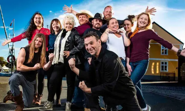 En glad grupp svenskar, kanske från en historia podd med Anders Lundin, poserar glatt utomhus.