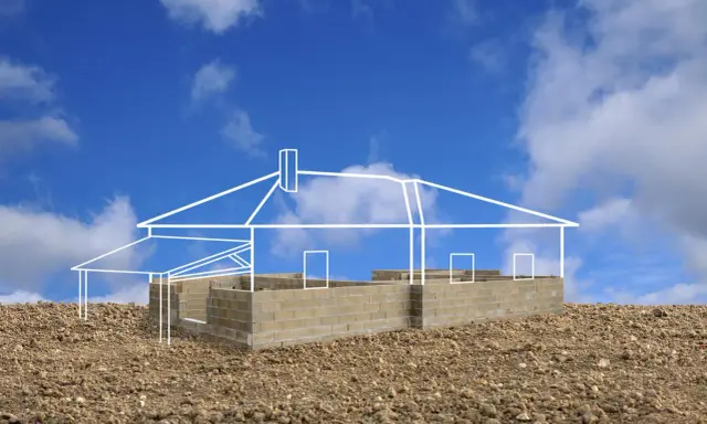 Esquisse d'une maison sur un terrain rocailleux, montrant les fondations en parpaings et le plan blanc de la structure. L'implantation maison sur terrain est en cours.