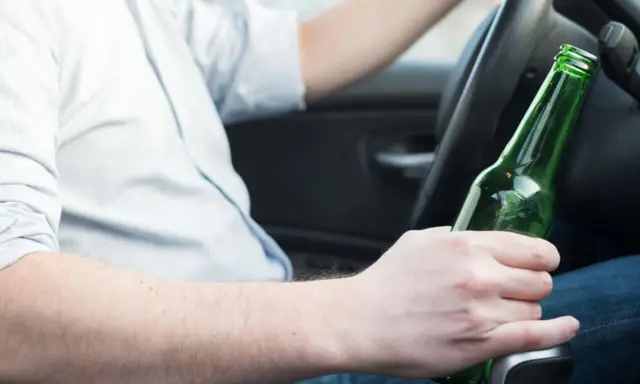 Mężczyzna za kierownicą trzyma butelkę piwa, zastanawiając się, ile promili ma jedno piwo.