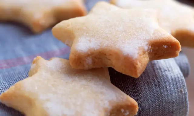 Des sablés au citron en forme d'étoiles, saupoudrés de sucre, reposent sur un tissu bleu.