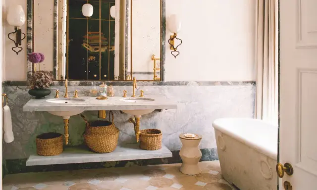 Elegante baño con doble lavabo de mármol, bañera exenta y suelo de baldosas. Un espejo con marco dorado y un cuadro oriental añaden un toque de lujo. ¡Ideas para pintar azulejos baño!