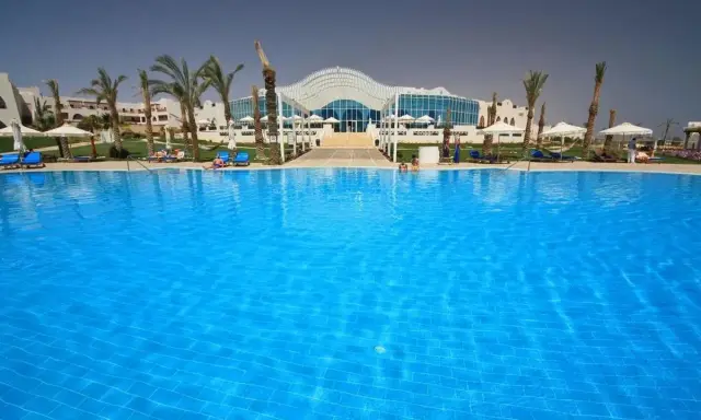 Basen w Hilton Marsa Alam Nubian Resort. Wiele osób odpoczywa na leżakach pod palmami.