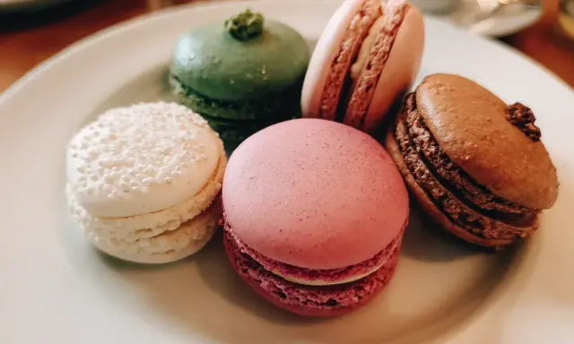 Fem färgglada macarons på en tallrik. En vit med pärlor, en grön, en rosa, en ljusrosa och en brun. Perfekt för ett macarons recept.