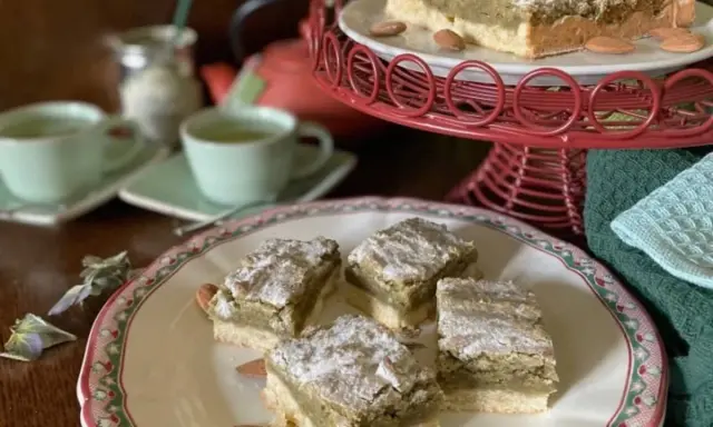 Carrés de croute à thé aux amandes, saupoudrés de sucre glace, servis avec des tasses de thé vert.