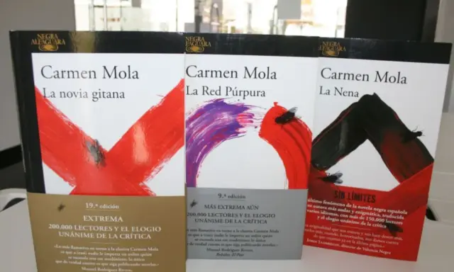Libri di Carmen Mola: "La novia gitana", "La Red Púrpura" e "La Nena". Copertine con disegni astratti e mosche.