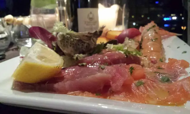 Un piatto di pesce crudo, con salmone, tonno e scampi, accompagnato da limone e insalata. Un'ottima occasione per degustazioni gastronomiche.