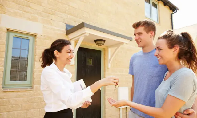 Une agent immobilier remet les clés d'une maison à un jeune couple. Ils sont heureux d'acquérir leur nouveau logement, peut-être grâce au droit de préemption locataire.