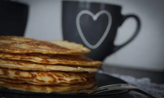 Stapel goldbrauner, **high protein pancakes** auf schwarzem Teller, daneben eine Tasse mit Herz.
