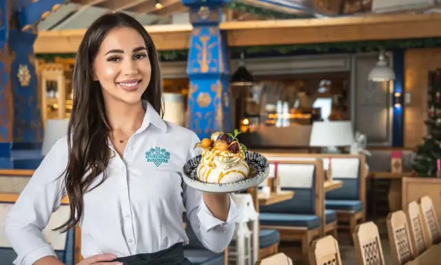 Kelnerka prezentuje deser z menu Schroniska Smaków Bukowina. Wnętrze restauracji zdobią góralskie wzory.