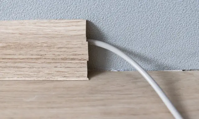 Une plinthe en bois imite le bois et cache un fil électrique. Astuce pour comment cacher des fils électriques.