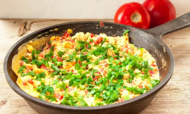 Pyszny omlet z warzywami, posypany szczypiorkiem, gotowy do podania. Obok leżą dwa pomidory.
