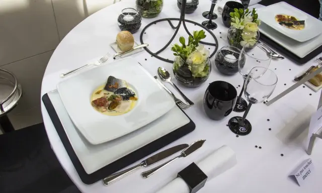 Une table de restaurant dressée avec élégance, un plat de poisson en vedette, des verres noirs et des fleurs.