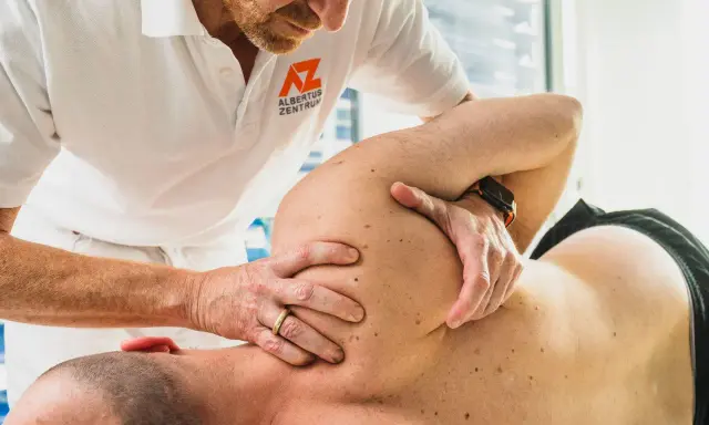 Therapeut führt eine gezielte Massage bei Schulterschmerzen durch. Hände des Therapeuten bearbeiten den Schulterbereich eines liegenden Patienten.