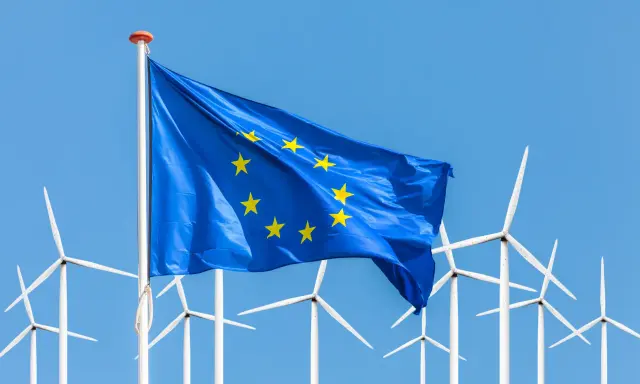 Europäische Flagge weht vor einer Reihe von Windrädern, die für erneuerbare Energien in der EU stehen.