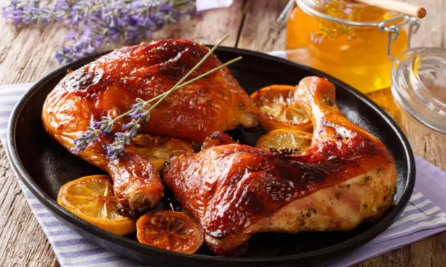 Muslos de pollo al horno dorados, servidos con rodajas de limón y un tarro de miel.