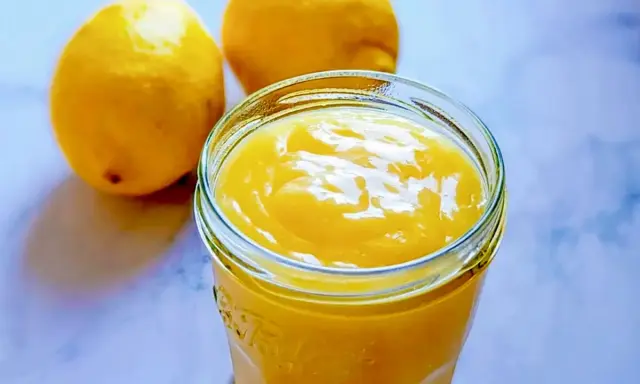 Un pot de lemon curd sans maïzena, onctueux et doré, à côté de deux citrons frais. Parfait pour une touche acidulée.