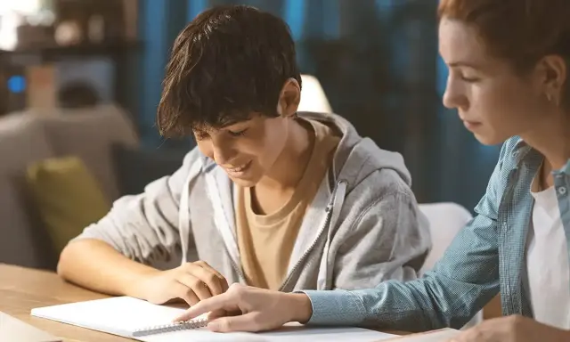 Ein Schüler gibt einem jüngeren Jungen Nachhilfe. Beide sind konzentriert und lernen gemeinsam.