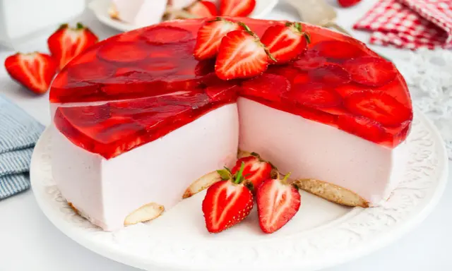 Pyszny sernik na zimno z mascarpone, udekorowany galaretką i świeżymi truskawkami. Idealny na letnie popołudnie.