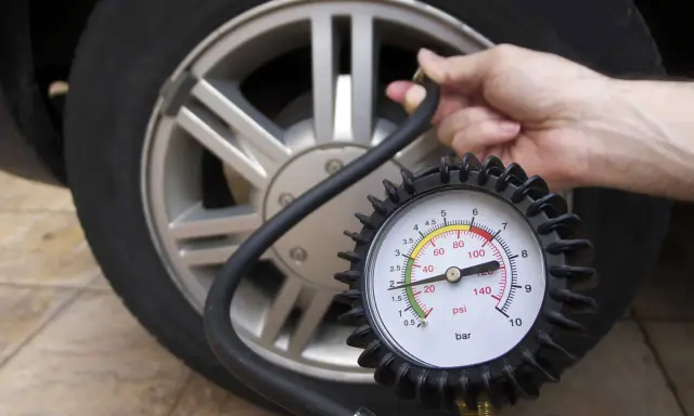 Controllo della pressione gomme auto con manometro. La lancetta indica un valore basso, suggerendo la necessità di gonfiare.