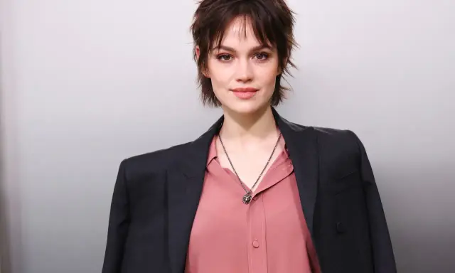 Junge Frau mit modischer Kurzhaarfrisur, inspiriert von Frisuren ab 50. Sie trägt einen rosafarbenen Blusen- und dunklen Blazer-Look.