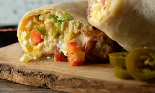 Pyszna tortilla z jajecznicą, pomidorami i papryką, podana na drewnianej desce z plasterkami jalapeno.