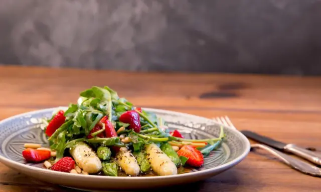 Ein frischer Spargelsalat mit Erdbeeren, Rucola und Pinienkernen, appetitlich auf einem Teller angerichtet.