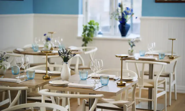 Vackert dukade bord med blåa glas och blommor i vaser, redo för gäster på en av restaurangerna i Skagen.