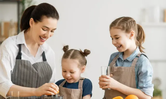 Mama z córkami robi sok pomarańczowy. To pyszne źródło witaminy A dla dzieci, które wspiera ich rozwój i odporność.