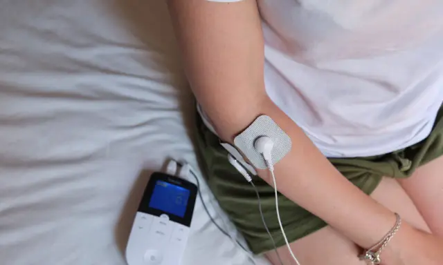 Traitement d'une épicondylite, maladie professionnelle, avec un appareil d'électrostimulation sur le bras.