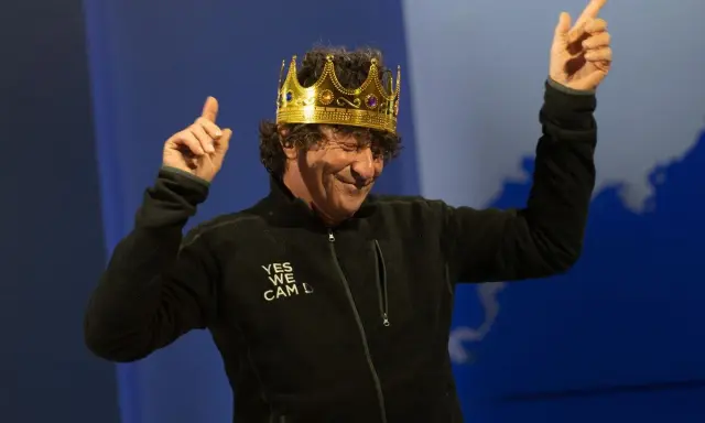 Jean Le Cam, le roi des mers, porte une couronne dorée et une veste noire avec l'inscription "YES WE CAM L".