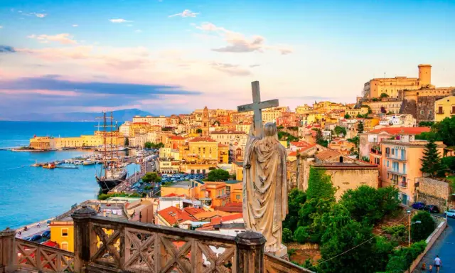 Una statua con una croce domina la vista di una città costiera colorata, perfetta per una gita fuori porta da Roma.
