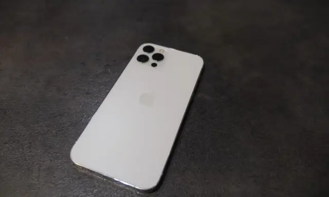 Elegancki, biały iPhone 12 Pro Max z charakterystycznym modułem aparatów na ciemnym tle.