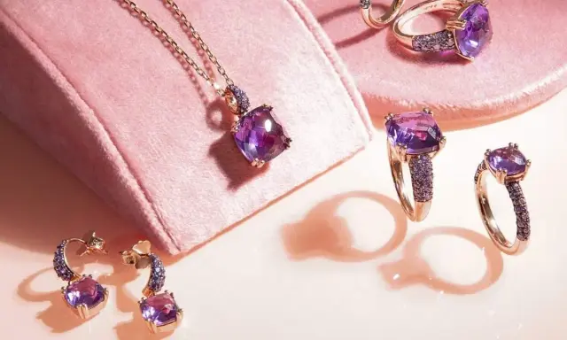 Gioielli con pietre viola intenso, un magnifico **ametista colore** che brilla su anelli, orecchini e una collana, su un morbido sfondo rosa.