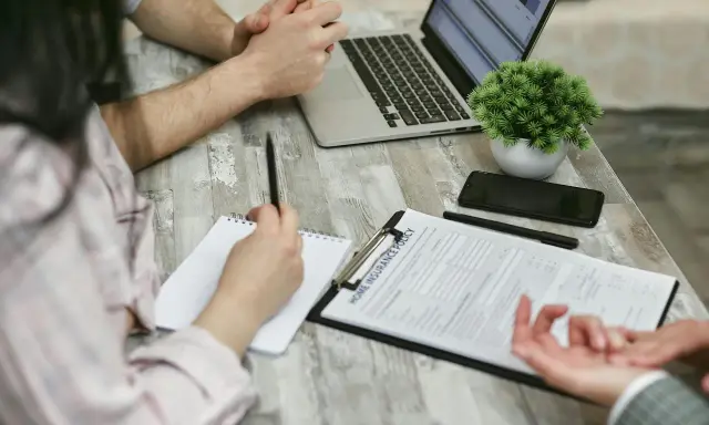 Réunion pour une contre-expertise assurance : un contrat est sur la table, un ordinateur portable ouvert, et des mains discutent des détails.
