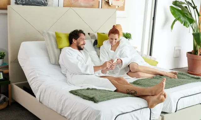 Pareja en bata blanca sobre cama articulada, aprendiendo como vestir una cama articulada para mayor comodidad.