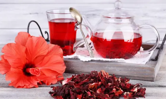 Orzeźwiająca herbatka z hibiskusa, podana w szklanym dzbanku i kubku, obok świeżego kwiatu i suszonych płatków.
