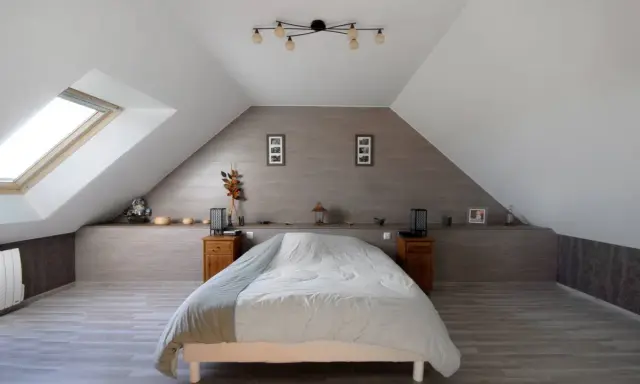 Chambre sous comble avec lit douillet, velux et décoration murale en bois.